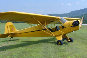 Bright yellow Piper J-3 Cub parked on a grassy field, used for taildragger and stick-and-rudder training.