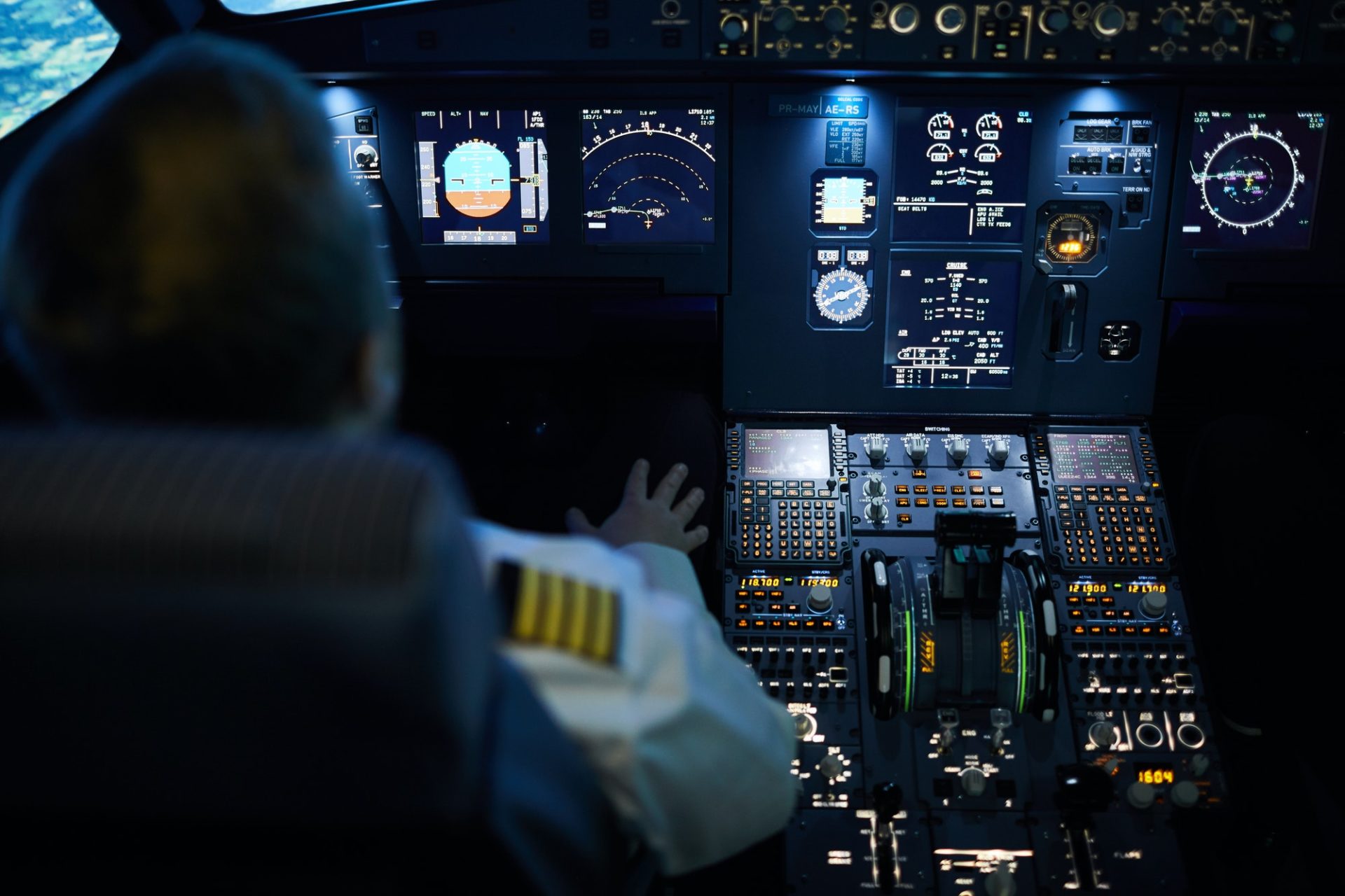 Pilot seated in a modern airliner cockpit, viewing illuminated flight instruments and navigation displays during instrument training